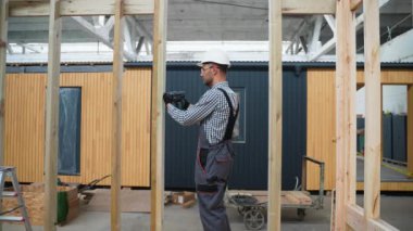 İşçi marangoz modüler bir ev monte ediyor. Fabrikadaki modern modüler evin yapımı. Matkap kullanan ve prefabrik konutların geliştirilmesi üzerinde çalışan işçiler