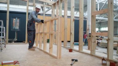 Üniformalı marangoz mühendisi inşaat alanındaki prefabrik modüler eve ahşap çerçeve kuruyor. Fabrikadaki modern modüler evin yapımı. Ekolojik ahşap konut kavramı