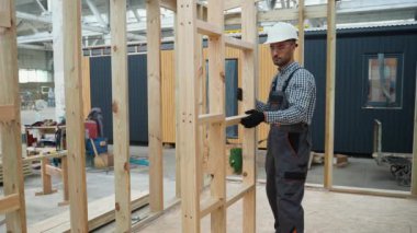 Üniformalı marangoz mühendisi inşaat alanındaki prefabrik modüler eve ahşap çerçeve kuruyor. Fabrikadaki modern modüler evin yapımı. Ekolojik ahşap konut kavramı