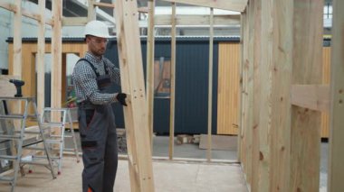 Üniformalı marangoz mühendisi inşaat alanındaki prefabrik modüler eve ahşap çerçeve kuruyor. Fabrikadaki modern modüler evin yapımı. Ekolojik ahşap konut kavramı