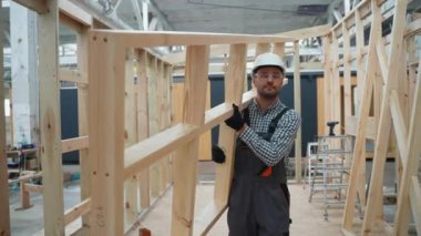 Üniformalı marangoz mühendisi inşaat alanındaki tamamlanmamış modüler evlerin içinden geçiyor. Fabrikadaki modern modüler evin yapımı. Ekolojik kavram