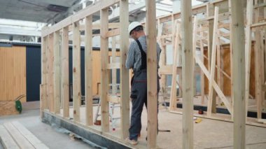 İşçi marangoz modüler bir ev monte ediyor. Fabrikadaki modern modüler evin yapımı. Matkap kullanan ve prefabrik konutların geliştirilmesi üzerinde çalışan işçiler
