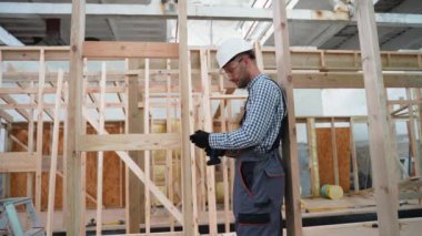 İşçi marangoz modüler bir ev monte ediyor. Fabrikadaki modern modüler evin yapımı. Matkap kullanan ve prefabrik konutların geliştirilmesi üzerinde çalışan işçiler
