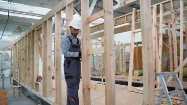 İşçi marangoz modüler bir ev monte ediyor. Fabrikadaki modern modüler evin yapımı. Matkap kullanan ve prefabrik konutların geliştirilmesi üzerinde çalışan işçiler