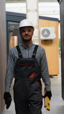 Modüler evin yakınındaki aletlerle gezen üniformalı bir pencere kurucusu. Bileşik ahşap panellerden yeni ve modern prefabrik modüler evler inşa ediliyor. Enerji verimli panel montajı