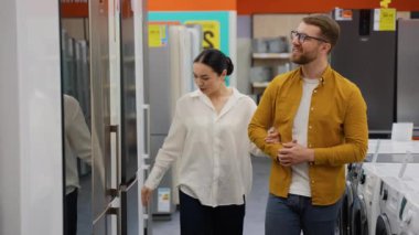 Alet gereçleri dükkanındaki buzdolabının kapısının açık olması ve yeni ev almak için diğer modellerle karşılaştırılması. Bir sürü buzdolabı var, seç ve al. Evli bir çift evi seçer.