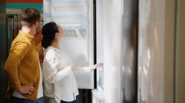 Genç çift yeni ev için tüketici elektroniği mağazasından buzdolabı seçiyor. Bir sürü buzdolabı var, seç ve al. Evli bir çift, ev aletlerini hipermarketten seçer.