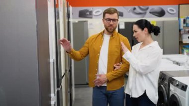 Genç çift ev aletleri mağazasında buzdolabına bakıyor. Bir sürü buzdolabı var, seç ve al. Evli bir çift, ev aletlerini hipermarketten seçer.