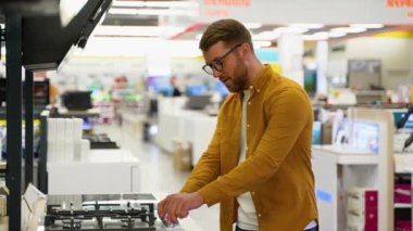 Komik adam, mobilya mağazasında DJ 'in gaz sobasında çalmasını taklit ediyor. Yakışıklı adam ev aletlerini hipermarketten seçiyor.