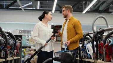 Elektrikli süpürge seçerken tartışan bir çift. Yeni teknoloji konsepti. Alışveriş zamanı eğleniyor. Ev aletleri mağazasında genç bir çift.