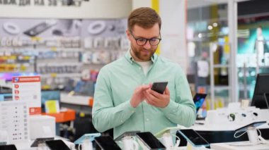 Mutlu genç adam teknoloji mağazasında yeni bir akıllı telefon seçiyor..