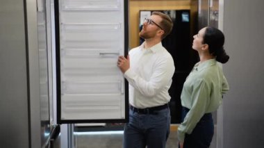 Tezgahtar, genç bir bayana eşyacı dükkanında buzdolabı seçmesinde yardım ediyor. Büyük satış, Kara Cuma konsepti.