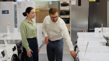 Tezgahtar, genç bir bayana alet edevat dükkanından çamaşır makinesi almasında yardım ediyor. Büyük satış, Kara Cuma konsepti.