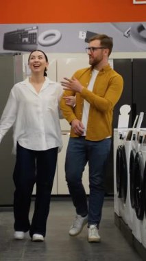 Hırdavatçıdaki genç çift ev için buzdolabı almayı seçiyor. Bir sürü buzdolabı var, seç ve al. Evli bir çift, ev aletlerini hipermarketten seçer.