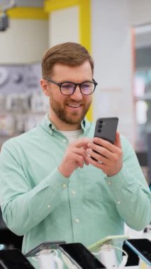 Teknoloji mağazasında yeni bir akıllı telefon seçen mutlu genç adam. Büyük satış, Kara Cuma konsepti.