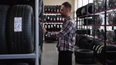 Bir adam araba tamirhanesinde kış lastiklerini seçer. Lastik, tekerlek ve otomobil parçaları satma kavramı