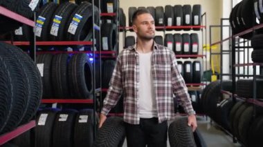 Oto yedek parça mağazasında yeni araba lastikleriyle yürüyen bir erkek satıcı. Otomotiv işi, otomobil parçaları satışı