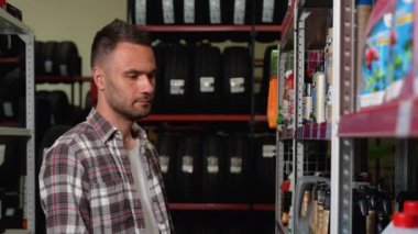 Bir adam araba tamirhanesinde araba yağı seçer. Otomotiv işi, otomobil parçaları satışı