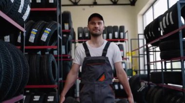 Oto yedek parça mağazasında yeni araba lastikleriyle yürüyen bir erkek satıcı. Otomotiv işi, otomobil parçaları satışı