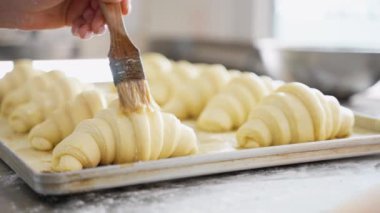 Kruvasanı fırında pişirmeye hazırlayın. Dişi fırıncı, çiğ kruvasanları fırçayla süpürür. Yemek pişirme süreci. Fırın yapımı taze pişmiş yiyecekler. Pastane Konsepti