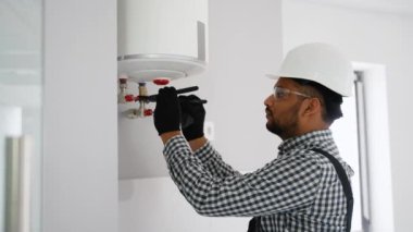 Hintli tesisatçı kazan ve boruları kontrol ediyor. Kazan dairesi bakım konsepti. Gaz kazanının tamiri