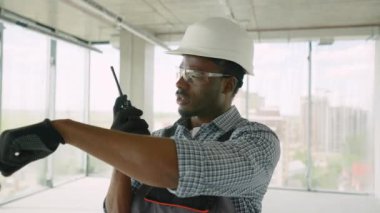 Afrika kökenli Amerikalı ustabaşı modern bir ofis inşa etmek için telsiz kullanıyor. İnşaat alanında telsizle konuşan bir inşaatçı var.