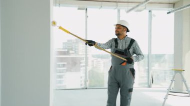 Ofiste duvar boyayan Hintli bir ressam. Asyalı müteahhit, inşaat alanının içindeki beton duvara astar beyaz boya yapmak için uzun saplı paten fırçası kullanıyor.