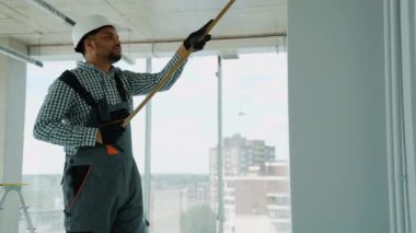 Ofiste duvar boyayan Hintli bir ressam. Asyalı müteahhit, inşaat alanının içindeki beton duvara astar beyaz boya yapmak için uzun saplı paten fırçası kullanıyor.