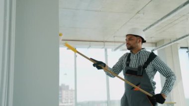 Ofiste duvar boyayan Hintli bir ressam. Asyalı müteahhit, inşaat alanının içindeki beton duvara astar beyaz boya yapmak için uzun saplı paten fırçası kullanıyor.