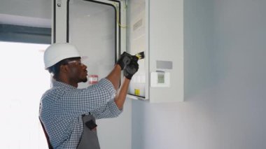 Afrikalı Amerikalı erkek elektrikçi elektrik kablosuyla santralde çalışıyor..