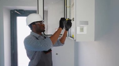 Afrikalı Amerikalı erkek elektrikçi elektrik kablosuyla santralde çalışıyor..