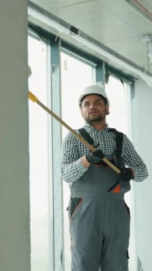 Ofiste duvar boyayan Hintli bir ressam. Asyalı müteahhit, inşaat alanının içindeki beton duvara astar beyaz boya yapmak için uzun saplı paten fırçası kullanıyor.