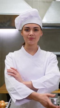 Mutfakta kollarını kavuşturmuş gülümseyen beyaz kadın şefin portresi.