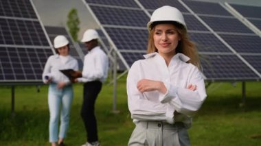 Güneş panelleriyle ekolojik yeşil alanda çalışırken kameraya bakan profesyonel kadın mühendisin portresi. Fotovoltaik elektrik santrali konsepti. Güneş panelleri enerji çiftliği. Fotovoltaik hücre parkı