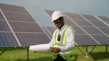 Şablonlu Afrikalı mühendis elektrikçi güneş panellerini kontrol ediyor. Fotovoltaik elektrik santrali konsepti. Güneş panelleri enerji çiftliği. Fotovoltaik hücre parkı, yeşil enerji konsepti
