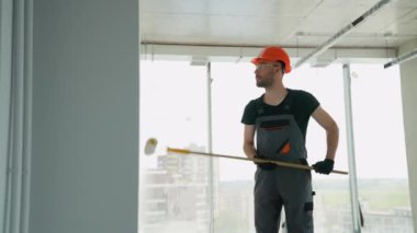 Ofiste duvar boyayan profesyonel bir ressam. İnşaat işçisi, inşaat alanının içindeki beton duvara astar beyaz boya yapmak için uzun saplı paten fırçası kullanıyor.