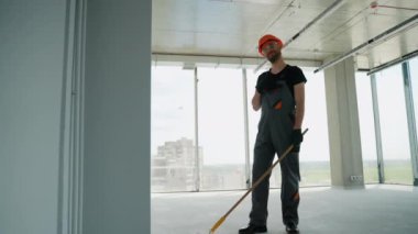 Ofiste duvar boyayan profesyonel bir ressam. İnşaat işçisi, inşaat alanının içindeki beton duvara astar beyaz boya yapmak için uzun saplı paten fırçası kullanıyor.