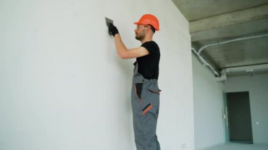 Duvarda sıva yapan inşaat işçisi. Tadilat işçileri duvarı alçılıyor. İnşaat işleri tamamlanıyor. Bir spatula duvarıyla aynı hizaya geliyor. Macun mala katmanının uygulanması işlemi