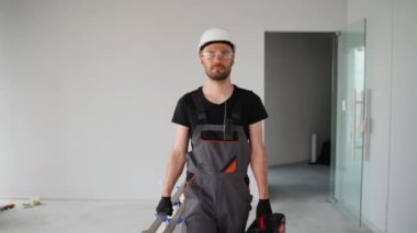 İnşaat işçisi üniformalı ve miğferli inşaat alanında aletlerle yürüyor.