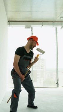 Komik inşaatçı inşaat alanında uzun kulplu fırçayla dans eder ve şarkı söyler. Profesyonel ressam ofiste bir duvar boyuyor.