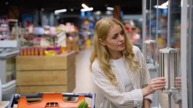 Bir kadın yiyecek dükkanından bıldırcın yumurtası alıyor. Markette alışveriş arabası taşıyan beyaz bir kadın, eşyalar seçiyor.