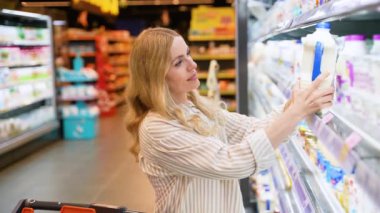 Güzel ev hanımı süpermarketten süt alıyor. Bir kadın marketin soğutuculu bölümünde alışveriş yaparken çeşitli tercihleri üzerine kafa yoruyor.