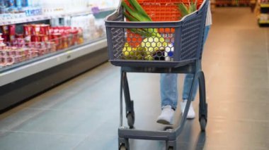 Alışveriş yapan bir kadın süpermarkette içi taze yiyeceklerle dolu bir alışveriş arabasını kendinden emin bir şekilde itiyor. İnsanlar gastronomi gıda konsepti satın alıyor.