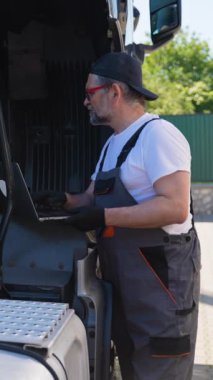 Atölyede kamyonun yanında çalışan tanısal alet dizüstü bilgisayarı olan bir araç tamircisi. Kamyon bakımı, servis ve onarım