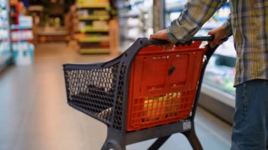 50 'li yaşlarda bir adam markette içi ıvır zıvır dolu bir alışveriş arabasını itiyor. Kafkasyalı bir adam, çeşitli ürünlerle dolu bir süpermarketin koridorlarından alışveriş yapıyor.