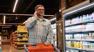 50 'li yaşlarda, market arabalı bir adam karısıyla telefonda konuşuyor, ne alacağını soruyor. Haftalık Alışveriş Konsepti