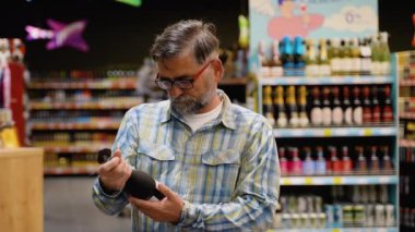 Kıdemli adam süpermarketten bir şişe lüks şarap seçiyor. Haftalık Alışveriş Konsepti