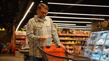 50 'li yaşlarda bir adam market fiyatlarındaki artış ve enflasyondaki kağıt kontrolünden şok olmuş gibi görünüyor. Haftalık Alışveriş Konsepti