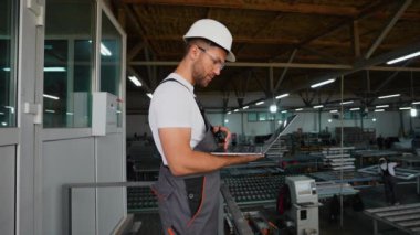 Dizüstü bilgisayarı ve telsizi olan ustabaşı PVC pencere fabrikasındaki işçilere emir veriyor. PVC pencere ve kapı üretimi