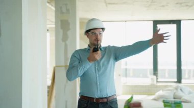 Telsiz kullanan ve inşaat alanında çalışan işçilere güvenlik kaskı takan bir mühendis.